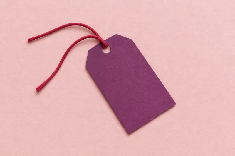 A plum paper gift tag with an untied cherry string, on blush pink paper.