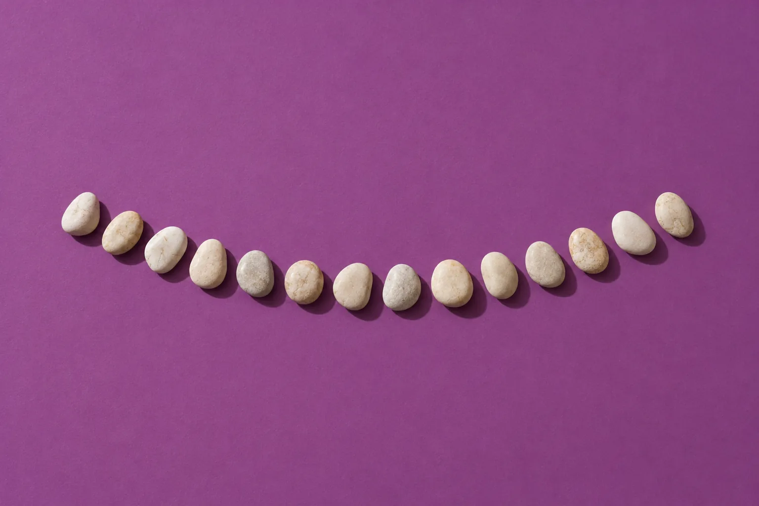 Fourteen smooth cream pebbles in a gentle curve on plum paper.