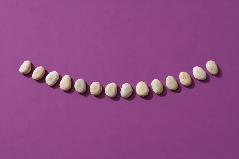 Fourteen smooth cream pebbles in a gentle curve on plum paper.