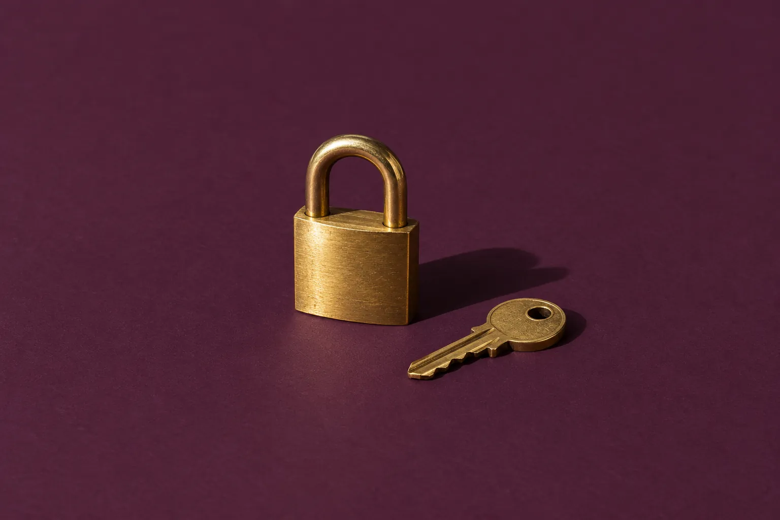 A small brass padlock with its key beside it, on deep aubergine paper.