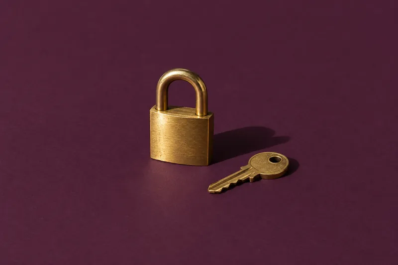 A small brass padlock with its key beside it, on deep aubergine paper.