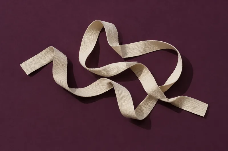 A loose, uneven loop of cream cotton ribbon on deep aubergine paper.