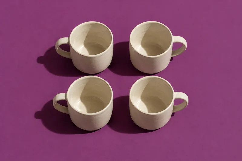 Four cream ceramic cups in a two-by-two grid on plum paper, seen from above.