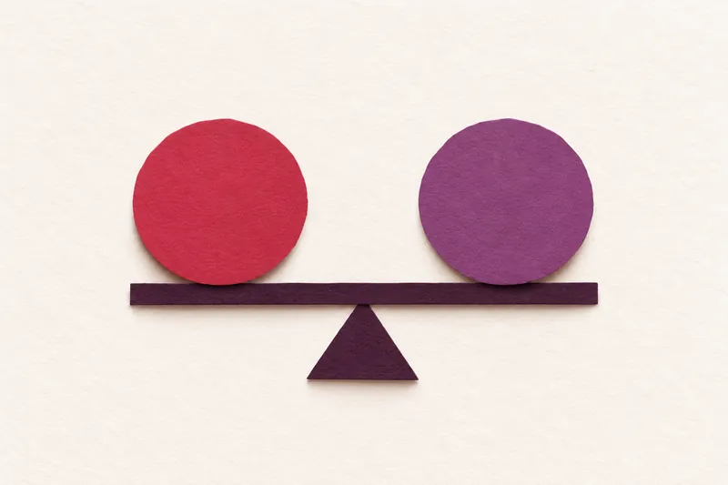 A cherry paper circle and a plum paper circle balanced on an aubergine beam, on cream paper.
