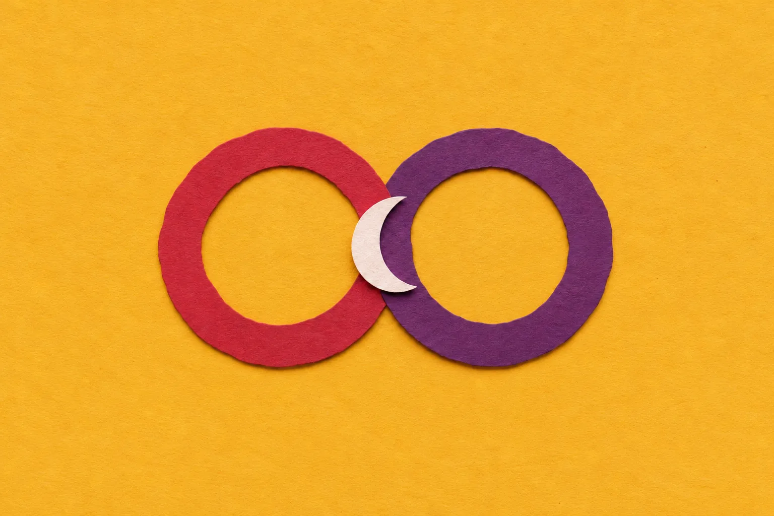 Two cut-paper rings, one cherry and one plum, overlapping on mustard paper, with a small cream crescent between them.