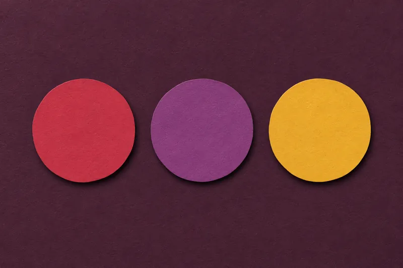 Three paper discs in cherry, plum and mustard in a row on aubergine paper.