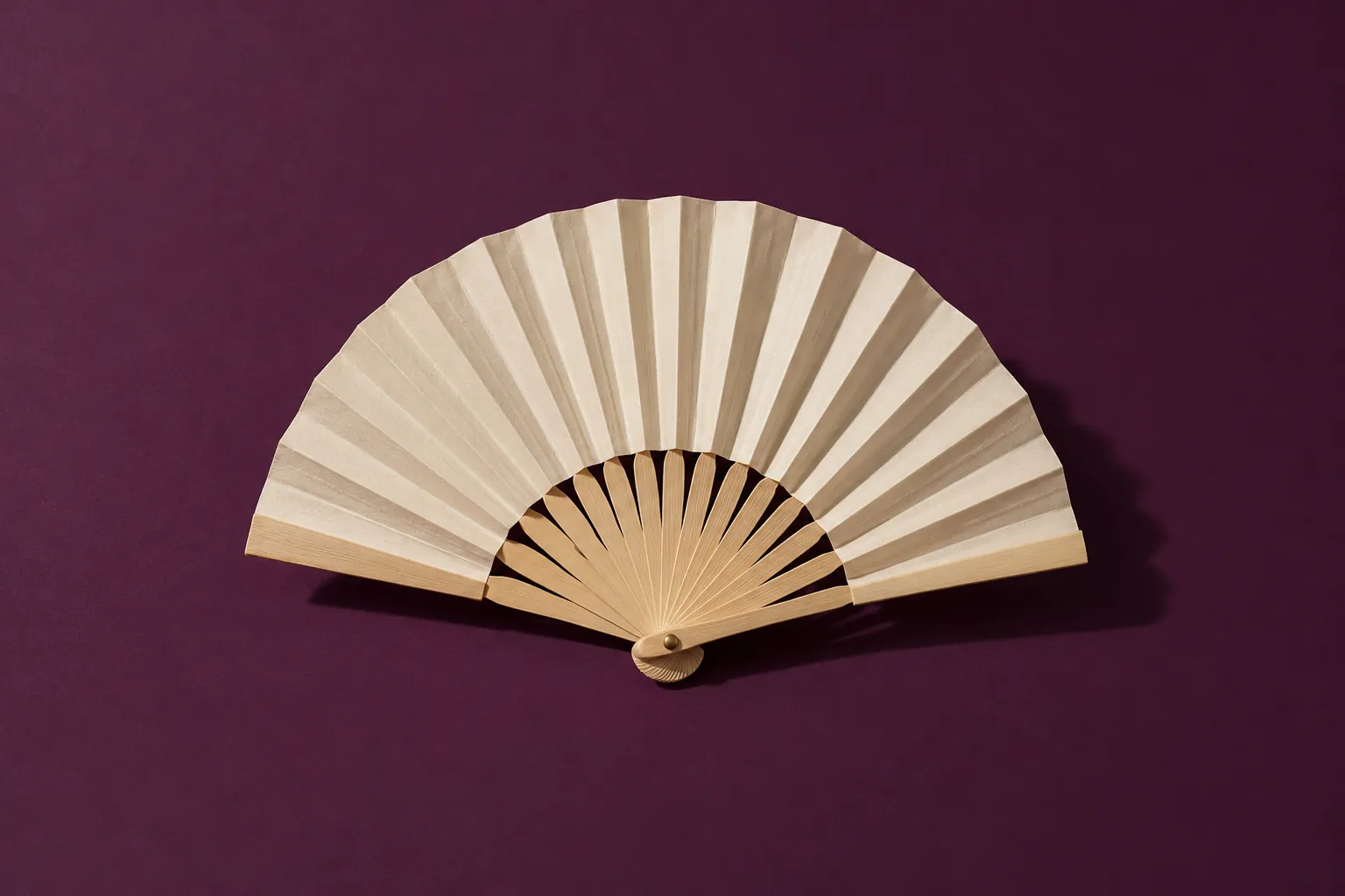 A cream paper hand fan, half open, on deep aubergine paper.