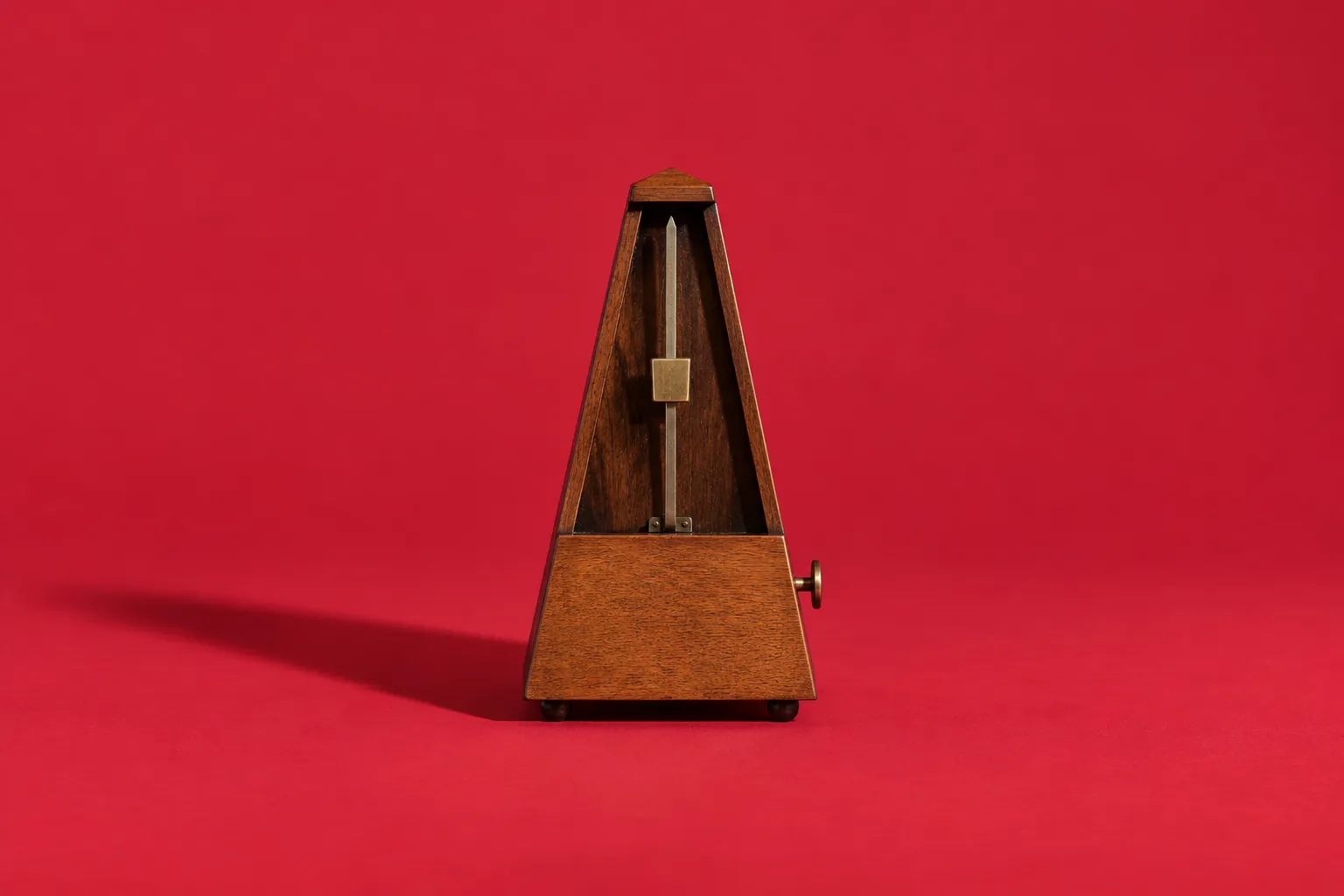 A small wooden metronome standing upright on cherry-red paper.