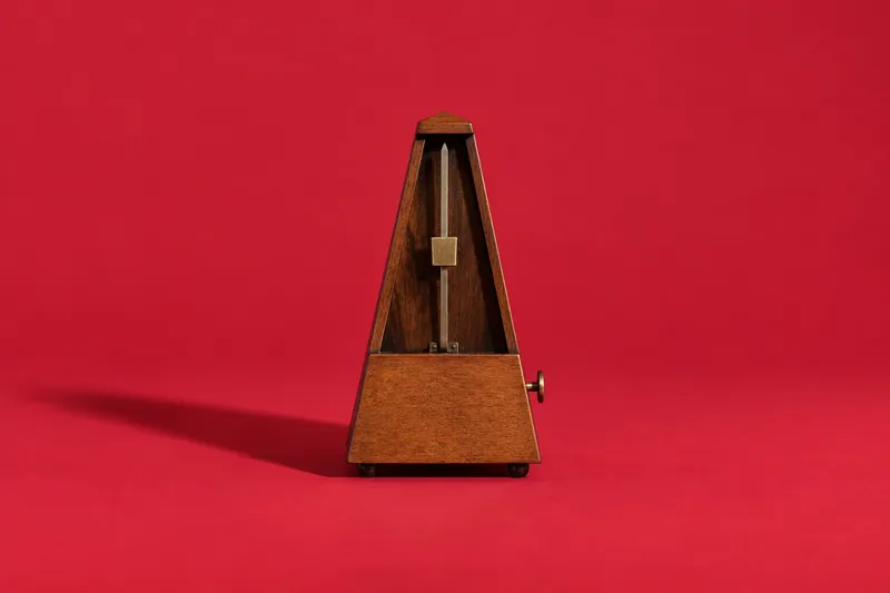 A small wooden metronome standing upright on cherry-red paper.