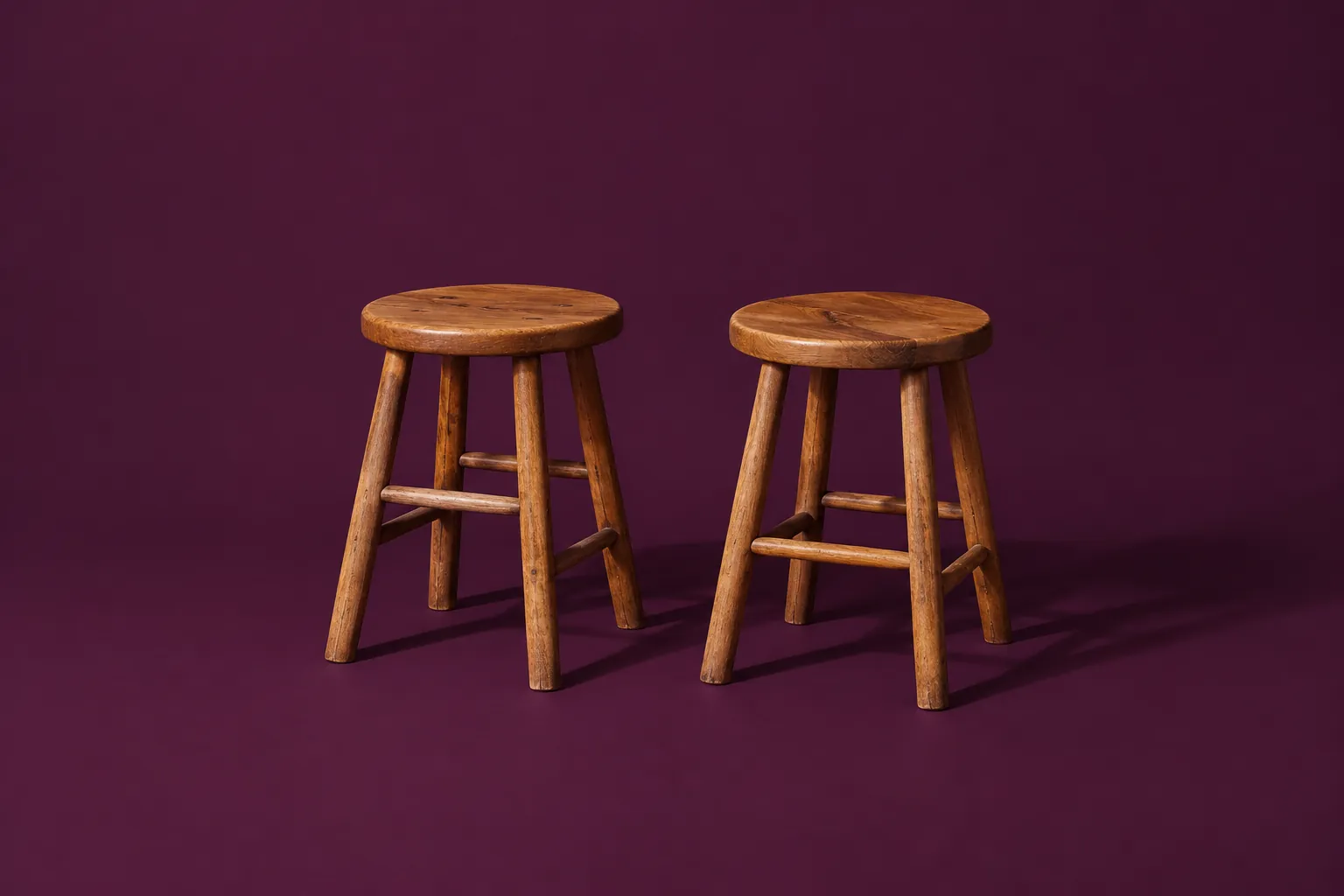 Two wooden stools side by side on deep aubergine paper.