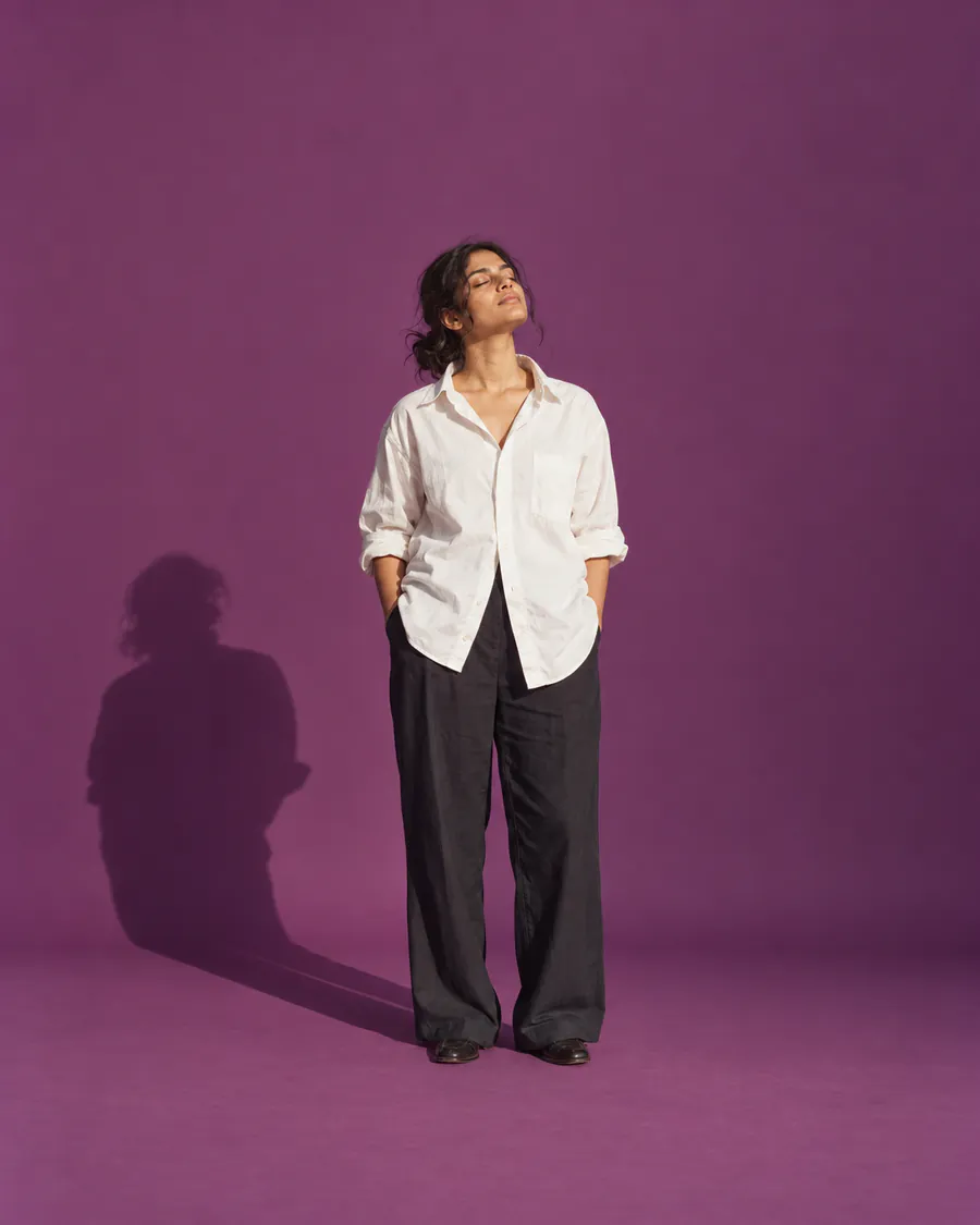 A woman in a white shirt stands with her eyes closed and her face turned up to the sun, against plum paper.