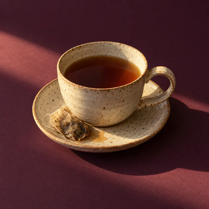 A cup of cold tea on a saucer in a beam of evening light on dark aubergine paper.