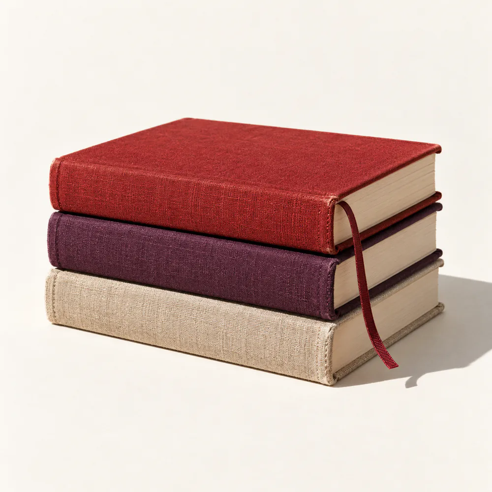 Three cloth-bound books in cherry, plum and oatmeal, stacked.