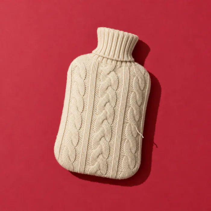 A cream knitted hot water bottle on cherry-red paper.