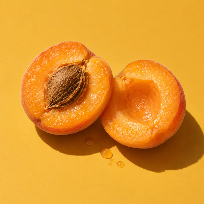 A ripe apricot split in two on mustard-yellow paper.